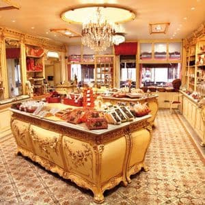 L'interno sfarzoso di un'antica cioccolateria con mobili dorati, un pavimento piastrellato ed espositori di dolciumi.