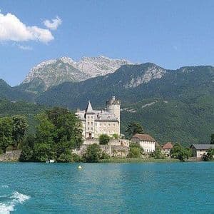Un castello di pietra si erge su un'isola boscosa in un lago turchese, con grandi montagne coperte di foreste sullo sfondo.