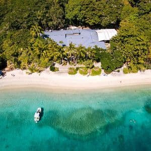 Une vue aérienne d'un littoral tropical avec une plage de sable blanc, une eau turquoise, un bateau et un bâtiment caché dans la forêt.