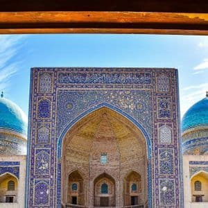 Una moschea ornata con cupole blu e un grande ingresso ad arco, vista attraverso due porte di legno aperte e finemente intagliate.