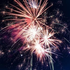 Esplosioni di fuochi d'artificio rossi e bianchi illuminano il cielo notturno scuro con scie e scintille luminose.