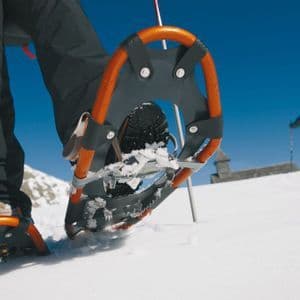 Primo piano di una ciaspola arancione che si solleva dalla neve durante un viaggio di gruppo WeRoad su una montagna soleggiata.