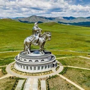 Una veduta aerea di una gigantesca statua equestre argentata in cima a un edificio circolare, sullo sfondo di verdi colline ondulate e montagne.
