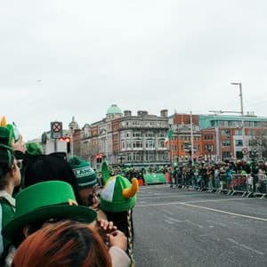 Un voyage de groupe WeRoad observe un défilé derrière des barricades, avec de nombreuses personnes portant des chapeaux verts.