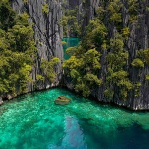 Una vista aerea di una caletta appartata con acqua cristallina e turchese, circondata da imponenti scogliere rocciose ricoperte di alberi.