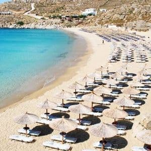 Vista dall'alto di una spiaggia sabbiosa fiancheggiata da file di ombrelloni di paglia e sedie a sdraio accanto a un'acqua limpida e turchese.