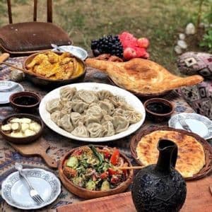 Un tavolo apparecchiato all'aperto con un banchetto di piatti tradizionali georgiani come i khinkali, pane, insalata, stufato e frutta fresca.
