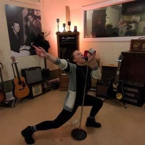 Una persona in posa canta in un microfono vintage all'interno di uno studio di registrazione musicale.