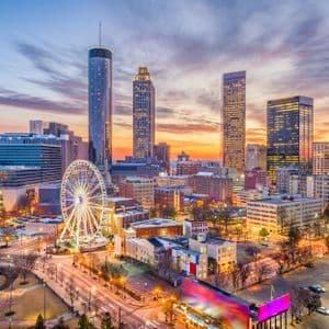 Un panorama urbain avec des gratte-ciel illuminés et une grande roue sous un ciel de coucher de soleil coloré.