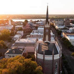 Vue aérienne d'une ville avec une église en briques et son clocher au coucher du soleil, avec une large rivière en arrière-plan.