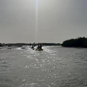Un gruppo WeRoad in silhouette che pagaia in kayak su un fiume calmo sotto un cielo luminoso e velato.