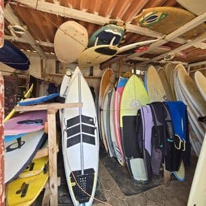 Decine di tavole da surf e mute riposte su rastrelliere e appese al soffitto di un rustico capanno da surf.