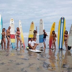 Un gruppo WeRoad posa con le tavole da surf su una spiaggia sabbiosa e bagnata con l'oceano sullo sfondo.