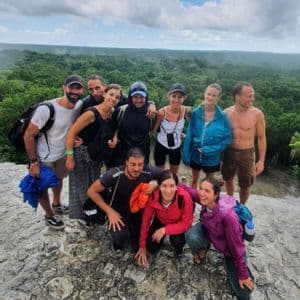 Un gruppo WeRoad in viaggio posa per una foto su un punto panoramico roccioso, con una vasta foresta verde che si estende sotto un cielo nuvoloso.