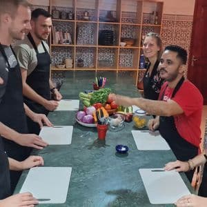 Eine WeRoad-Gruppe nimmt an einem Kochkurs teil, versammelt an einem großen Tisch mit frischem Gemüse und einem Kochlehrer.