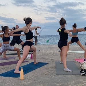 Eine WeRoad-Gruppenreise, die eine Yoga-Pose auf Matten auf einem Betonsteg am Meer unter bewölktem Himmel übt.