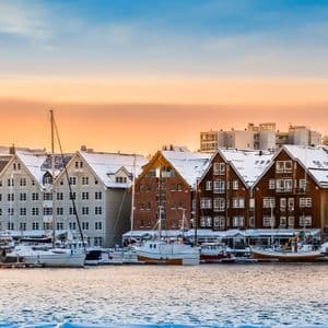 Un panorama de un puerto nevado con barcos amarrados a lo largo de un muelle bordeado de edificios tradicionales al atardecer.
