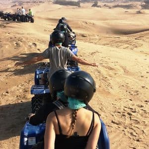 Eine WeRoad Gruppenreise, bei der ATVs in einer Reihe weite Wüstendünen durchqueren, von hinten gesehen.