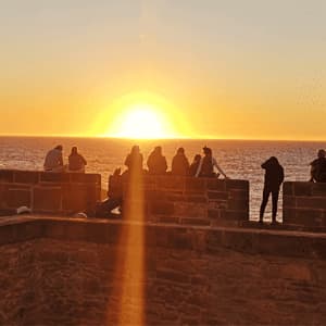 Silhouetten einer WeRoad-Gruppenreise, die den Sonnenuntergang über dem Meer von einer Steinmauer aus beobachten.
