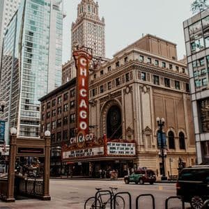 Una vista a nivel de calle del Teatro Chicago con su prominente letrero vertical, con un telón de fondo de rascacielos modernos y tráfico urbano.