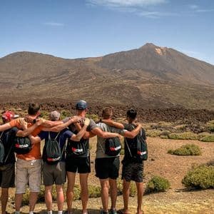 A WeRoad group trip of six men stand with their arms around each other, looking out at a vast volcanic mountain landscape.