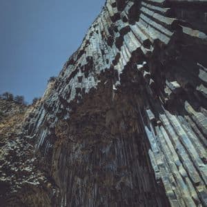 Vista dal basso di una grande formazione rocciosa con colonne esagonali di basalto contro un cielo azzurro limpido.