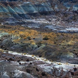 Un vasto paisaje de tierras baldías erosionadas con estratos coloridos de sedimento azul, gris y amarillo bajo la luz brillante del día.