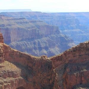 Acantilados de roca roja en primer plano enmarcan un cañón vasto y profundo con capas brumosas que se desvanecen en la distancia.