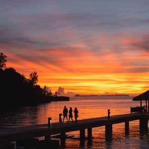 Sagome di un viaggio di gruppo WeRoad che camminano su un molo sul mare contro un tramonto vibrante arancione e viola.