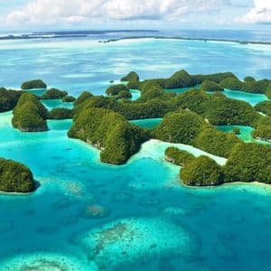 Vista aerea di un arcipelago tropicale con isole verdi lussureggianti sparse in un oceano turchese trasparente sotto un cielo nuvoloso.