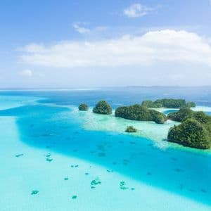 Una vista aerea di piccole isole rocciose coperte di vegetazione verde, sparse in un oceano turchese e blu intenso sotto un cielo parzialmente nuvoloso.