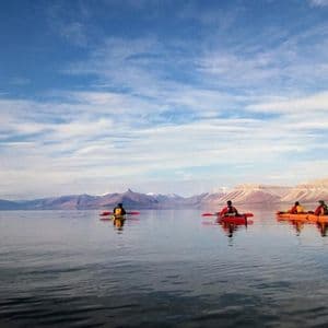 Un viaggio di gruppo WeRoad in kayak su un lago calmo di fronte a montagne innevate sotto un cielo parzialmente nuvoloso.