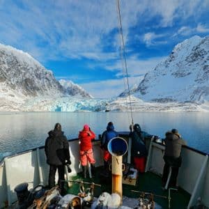 Un viaggio di gruppo WeRoad a prua di una barca osserva un grande ghiacciaio tra montagne innevate.