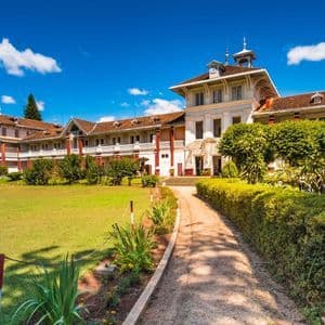 Ein Schotterweg führt durch einen gepflegten grünen Rasen zu einem großen Gebäude im Kolonialstil unter einem strahlend blauen Himmel.