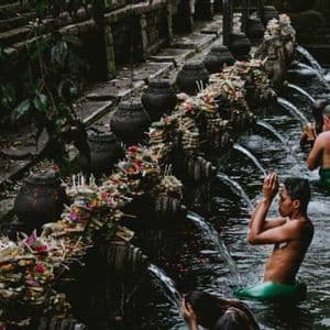 Un viaje en grupo de WeRoad participando en un ritual de purificación, bañándose bajo los chorros de agua de un templo de piedra.