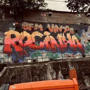 A colorful graffiti mural that says 'Bem Vindos Rocinha' on a concrete wall, with an orange municipal truck in the foreground.