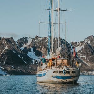 Un viaggio di gruppo WeRoad in barca a vela naviga acque calme con ghiacciai e montagne frastagliate e innevate sullo sfondo.