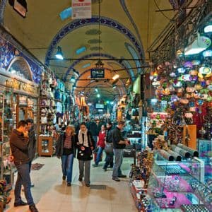 Le persone passeggiano in un affollato bazar al coperto con soffitti a volta, fiancheggiato da negozi che vendono lampade a mosaico colorate e souvenir.