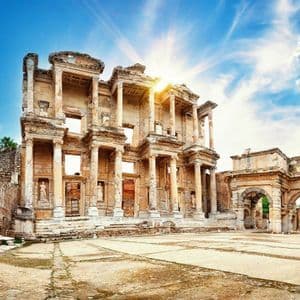 Il sole splende luminoso sulle antiche rovine di un grande edificio con colonne e archi in un cortile in pietra.