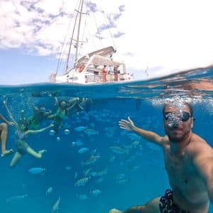 Un uomo si scatta un selfie subacqueo con il suo gruppo WeRoad mentre fa snorkeling tra un banco di pesci, con un catamarano in superficie.