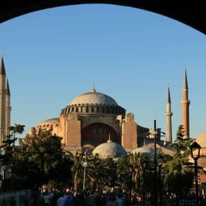 Una gran mezquita con múltiples cúpulas y minaretes, enmarcada por un oscuro arco contra un cielo azul claro al atardecer.