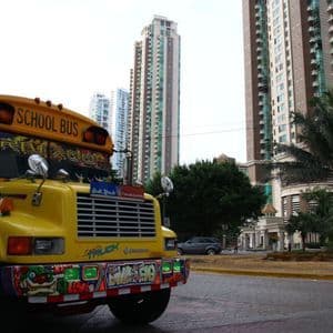 Un bus scolaire jaune, décoré de graffitis colorés, est garé dans une rue de ville devant de hauts bâtiments modernes.