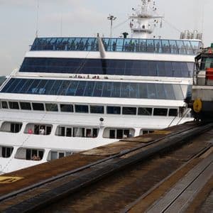 Une locomotive sur une voie tire un grand paquebot blanc à travers une écluse de canal tandis que les passagers regardent depuis les ponts supérieurs.