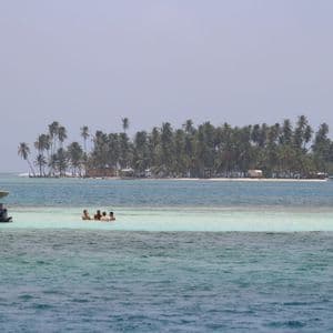Un voyage de groupe WeRoad nageant dans des eaux turquoise peu profondes près d'un bateau, avec une île couverte de palmiers au loin.