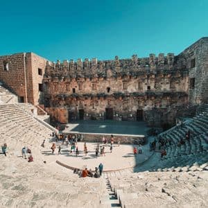 Un viaggio di gruppo WeRoad esplora le rovine di un grande anfiteatro in pietra sotto un cielo azzurro e luminoso.