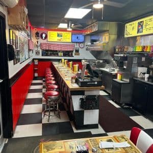 El interior de un diner americano de estilo retro con una barra larga, taburetes rojos y un suelo de cuadros blancos y negros.