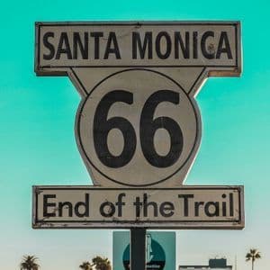 Un letrero clásico de la Ruta 66 en Santa Mónica que dice 'Fin del Sendero' contra un cielo azul turquesa despejado.