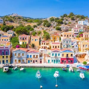 Edifici colorati fiancheggiano un porto in una giornata di sole, con barche ormeggiate nel mare limpido e turchese.