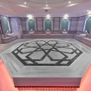 El interior de un moderno hammam turco con una gran plataforma octogonal de mármol decorada con un patrón geométrico en el centro.