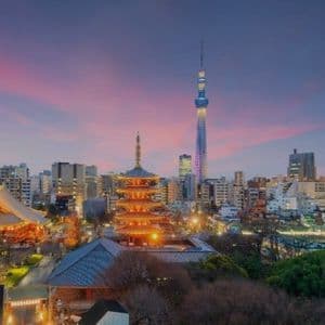 Un paesaggio urbano con pagode tradizionali illuminate e una torre moderna contro un cielo crepuscolare colorato.